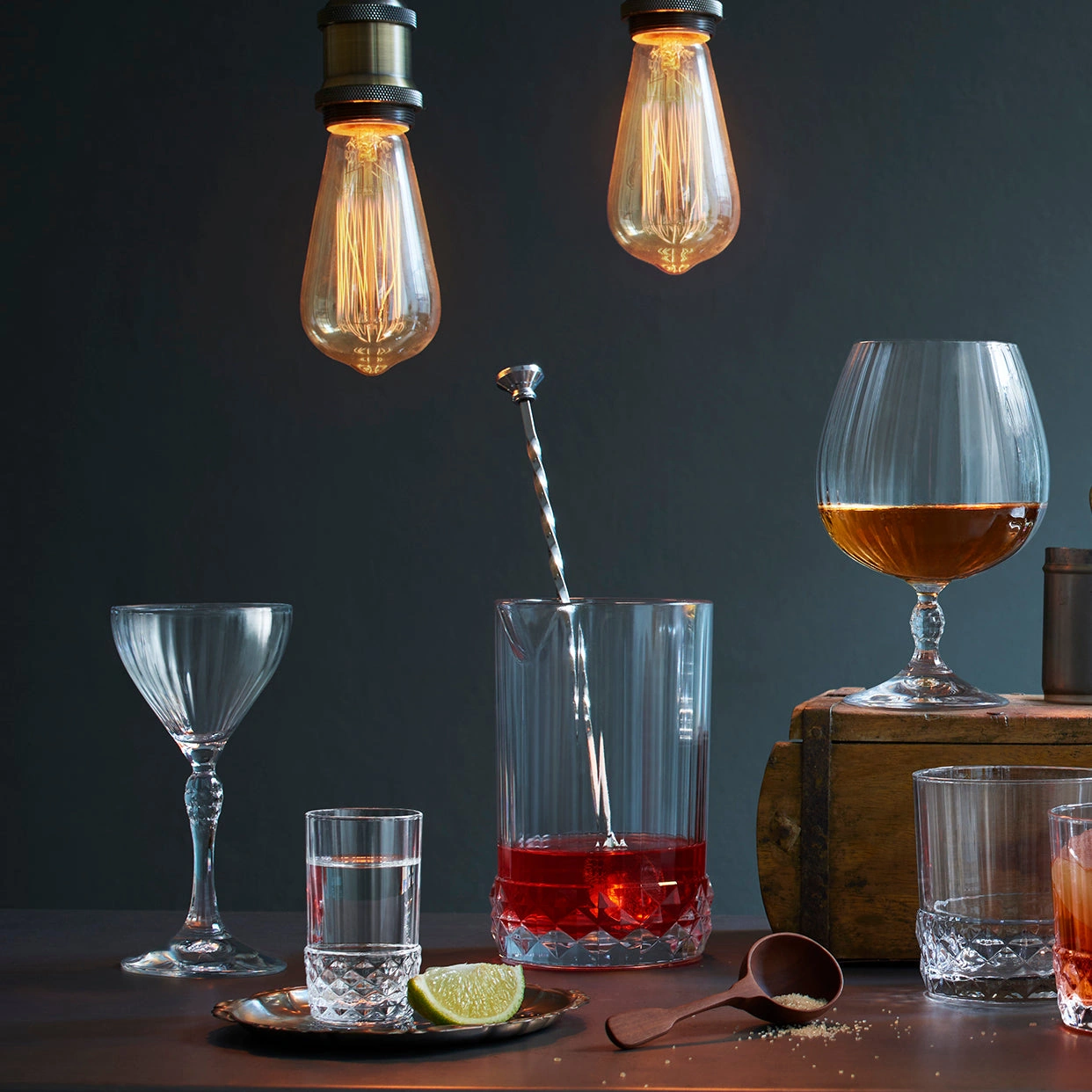 vaso mezclador de vidrio America: el vaso mezclador con la cuchara de bar en una barra de madera, entre los vasos de la línea America 20s