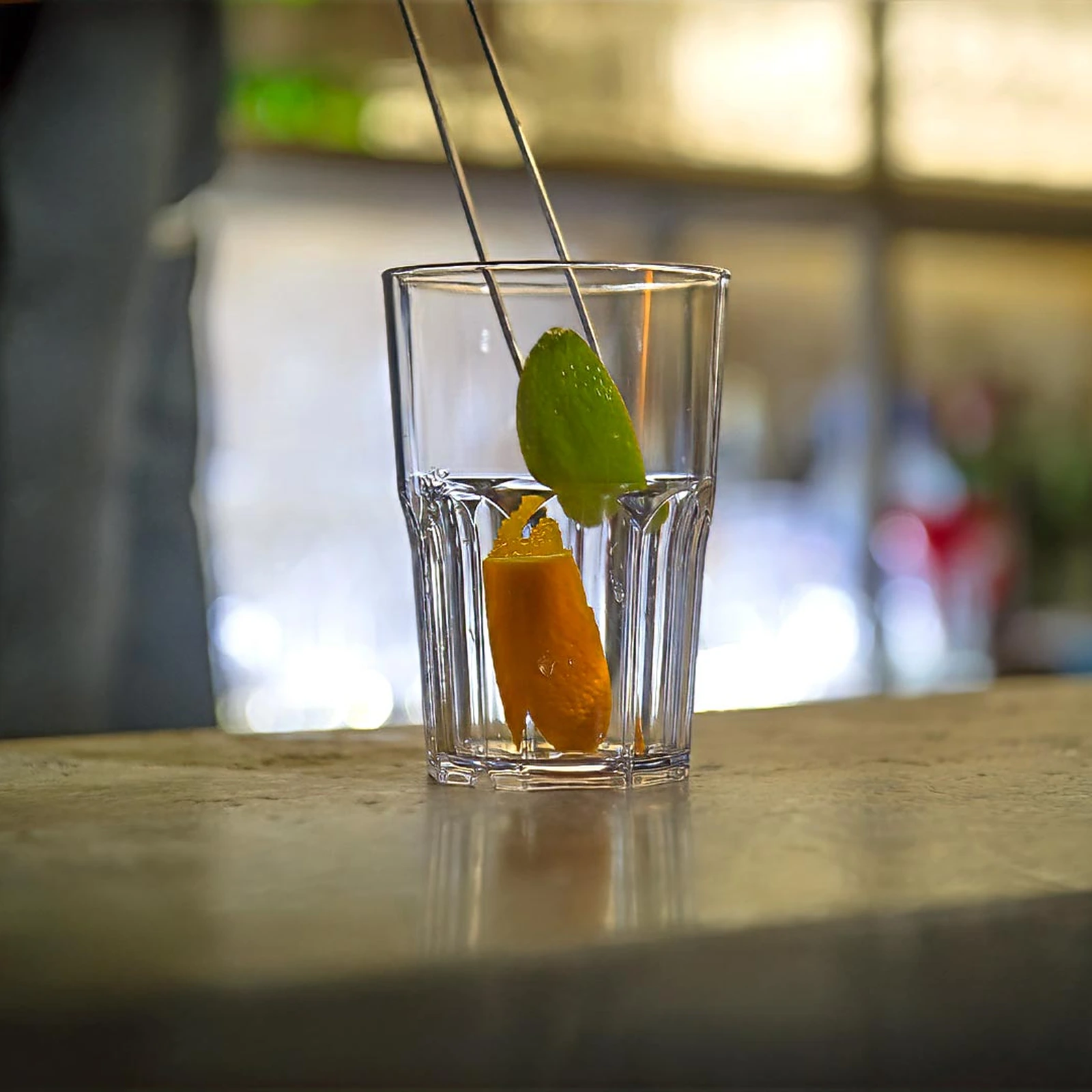 vaso irrompible Granity Clear de 40 cl sobre la barra, con piel de naranja y lima colocadas con la pinza de guarniciones