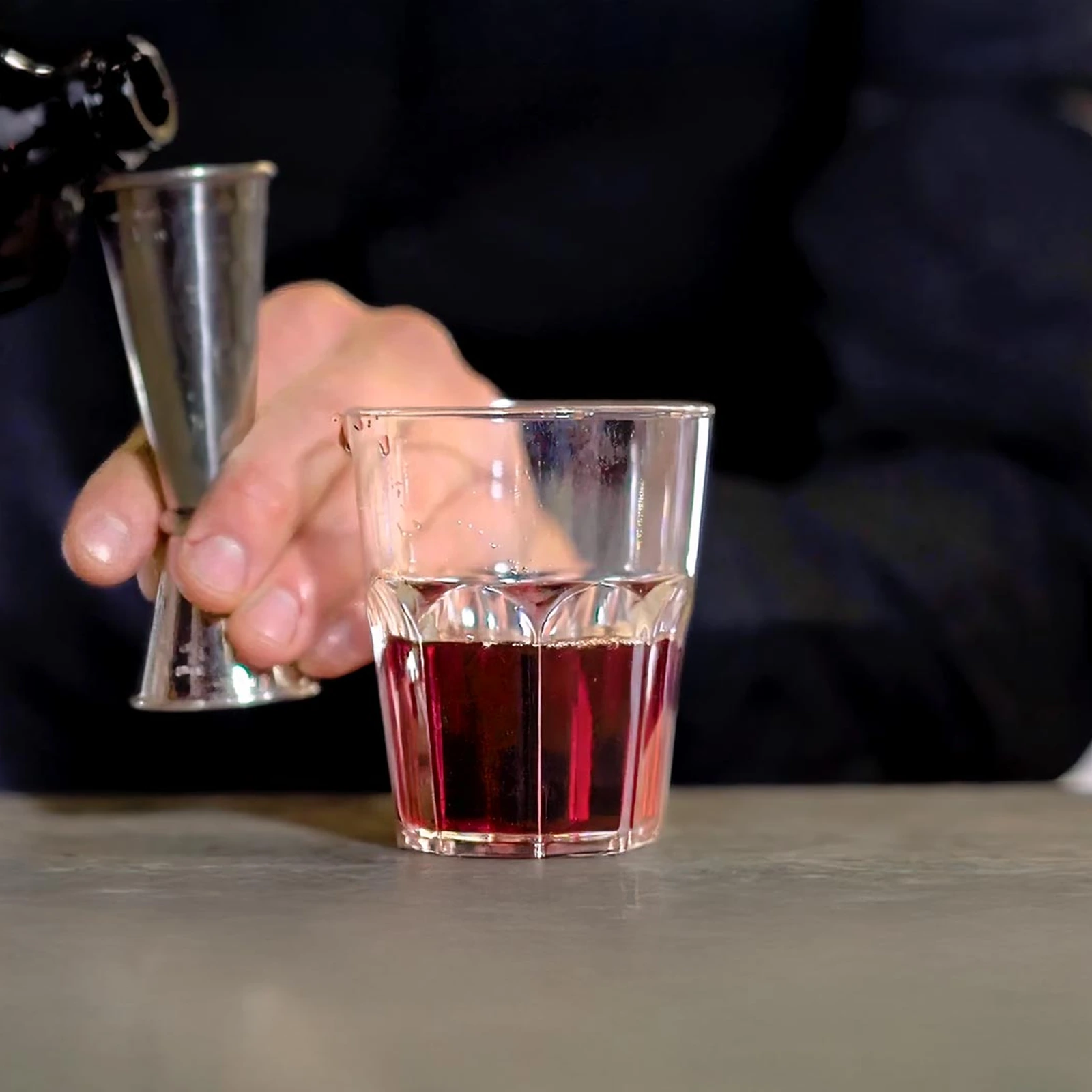 vaso reutilizable Granity Clear de 29 cl sobre la barra, mientras el bartender mide una bebida roja con el jigger